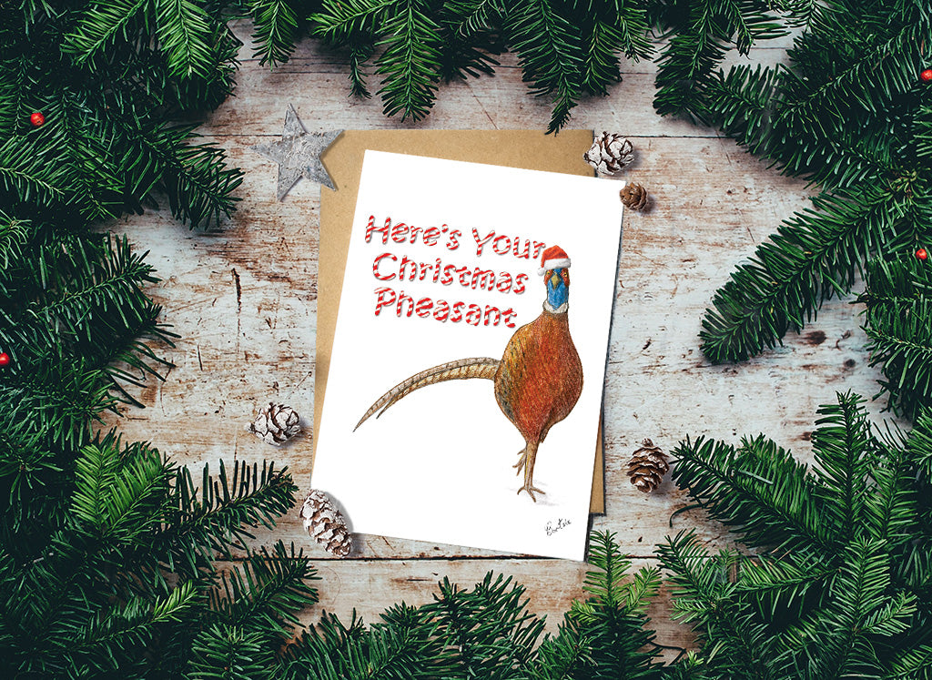 Here's your Christmas Pheasant card with pheasant illustration surrounded by pine branches on a wooden surface