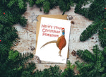 Here's your Christmas Pheasant card with pheasant illustration surrounded by pine branches on a wooden surface