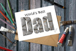 Card with 'World's Best Dad' text on a wooden surface with art supplies.