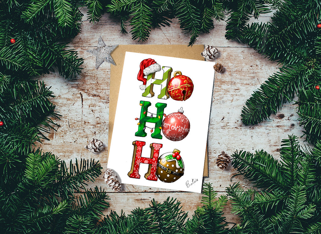 Christmas-themed card with decorative letters on a wooden surface surrounded by pine branches.