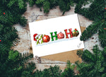 Christmas card with colorful ornaments spelling 'HO HO HO' surrounded by pine branches on a wooden surface.