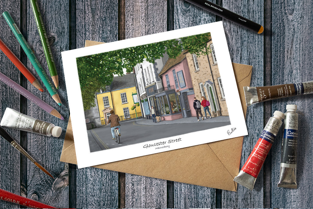 A Greetings card of an illustration of Gloucester Street, Malmesbury, with colorful buildings and people, 