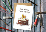 Greeting card with a cake illustration and text on a wooden surface with art supplies.